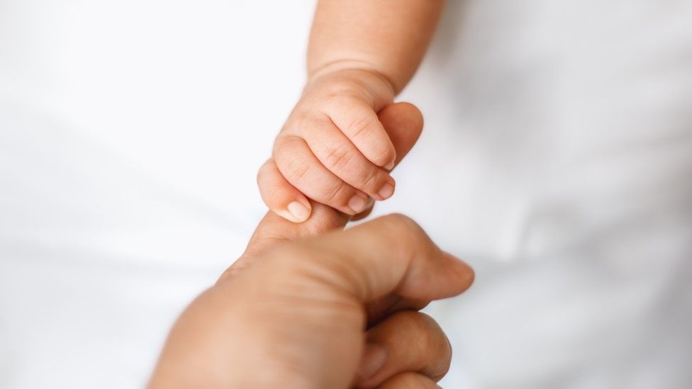 Newborn baby holding adult's finger