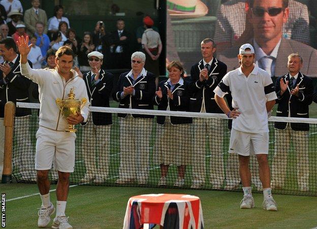 Federer celebrates his 2009 Wimbledon title, while a TV screen shows Sampras watching on from the stands