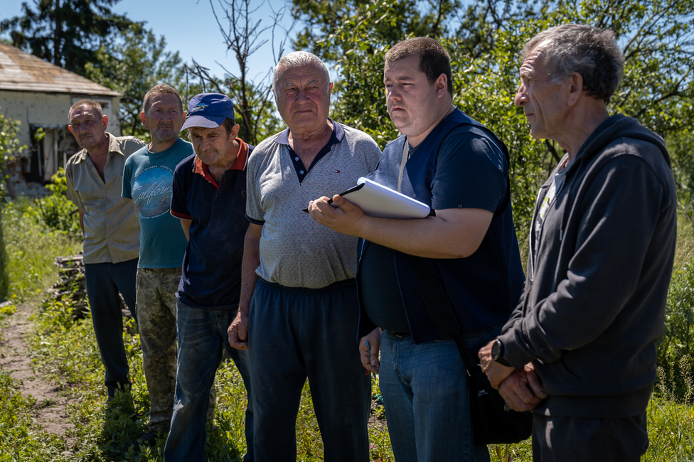 Vadym Bobaryntsev, right, watches on with other villagers as a member of the prosecutor's team takes notes in Mala Rohan.