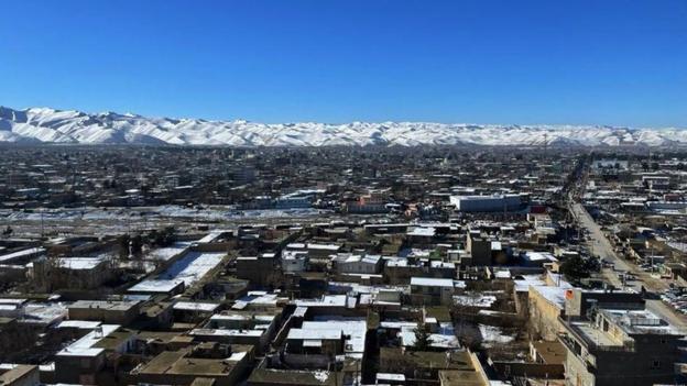 View of a small Afghan city, snow-topped mountains in the distance and a blue sky