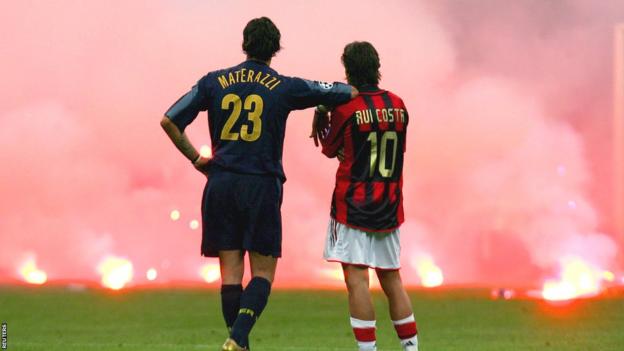 Marco Materazzi leans on the shoulder of Rui Costa as the pair watch smoke rise from flares thrown from the stands during the 2005 Champions League quarter-final between AC Milan and Inter Milan