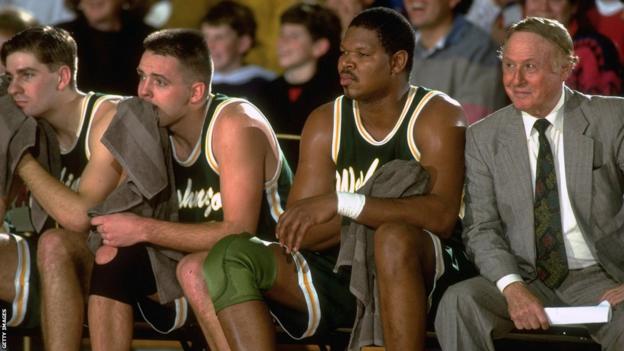 A suited Red Koltz sits on the bench alongside some tired, dejected looking Washington Generals players