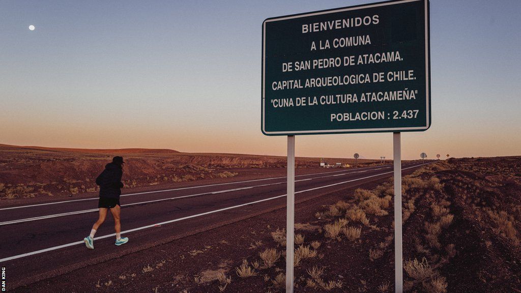 Tom Reynolds running past a sign welcoming visitors to the Atacama desert