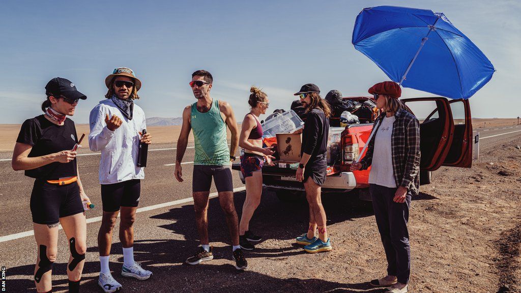 A team has a discussion on the roadside during The Speed Project. One holds a big blue beach umbrella