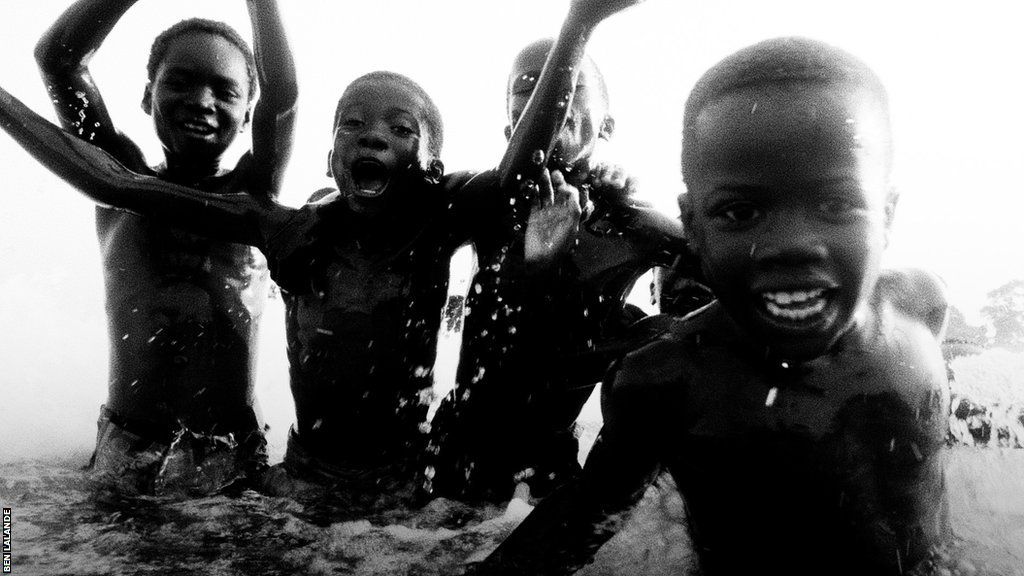 Four smiling boys play in the surf on the beach in Busua
