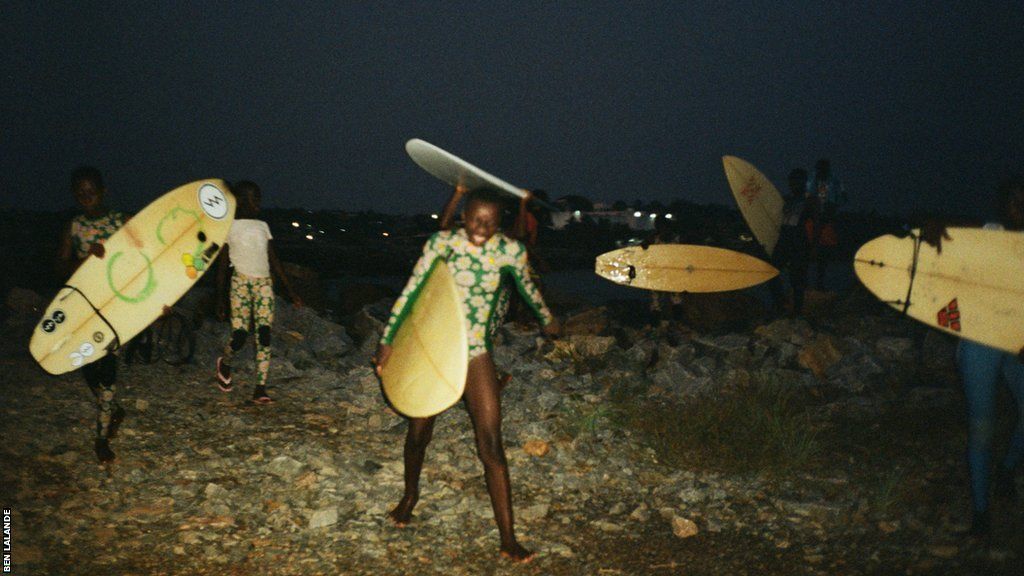 The Obibini Surf Club walk gingerly back across the beach with boards in hand as night falls